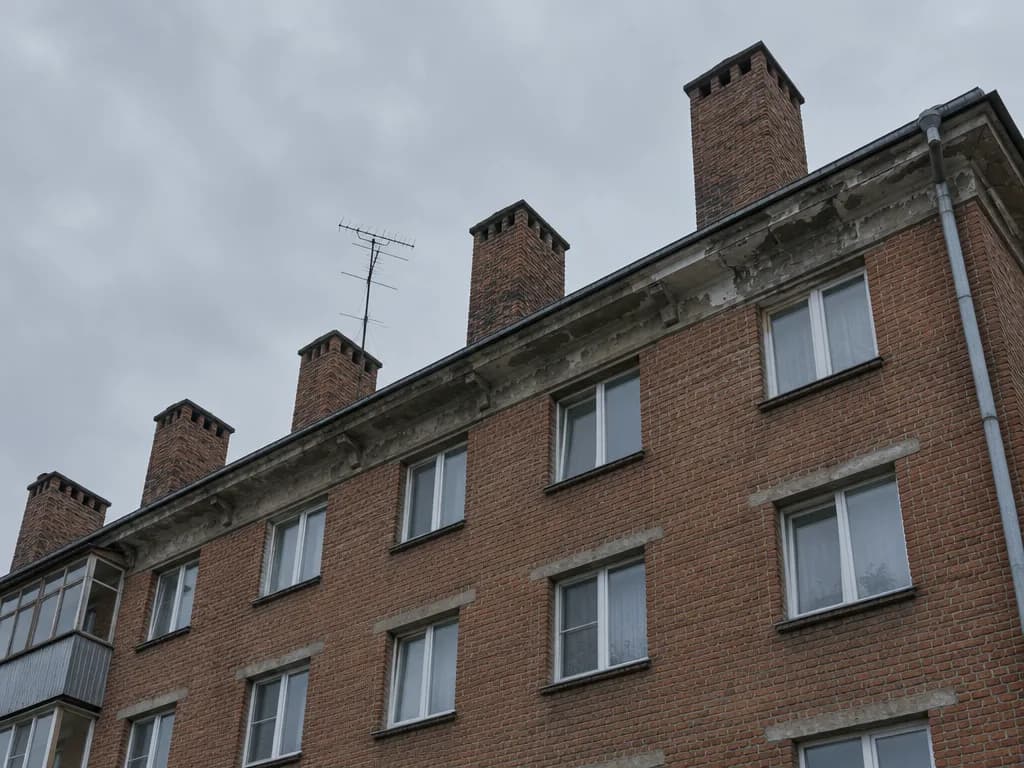 Nõukogudeaegse tellisest korterelamu katuseserv koos mitme korstnapiibuga, vaadatuna alt üles hallis sügisilmas