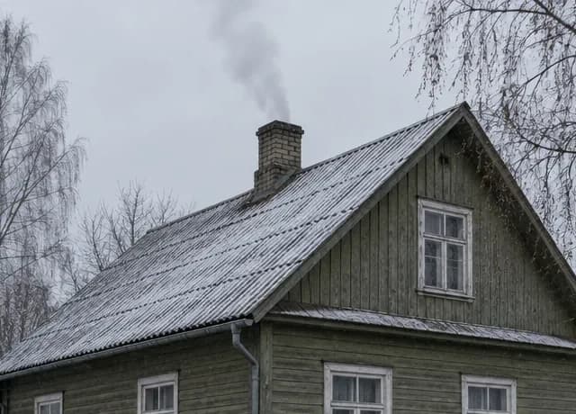Üksik Eesti puumaja varases talves, õhuke suits tellisest korstnapiibust hallil taevataustal